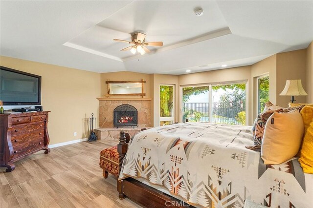 bedroom with ceiling fan, light hardwood / wood-style floors, access to exterior, and a tray ceiling