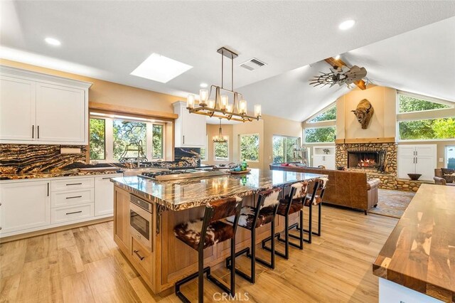 kitchen with white cabinets, a center island, lofted ceiling with skylight, and dark stone countertops