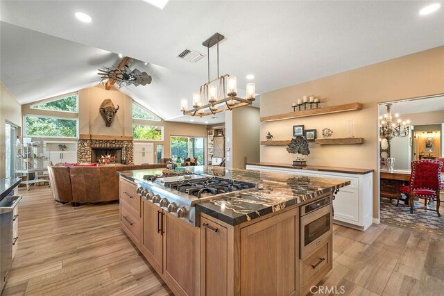 kitchen featuring light wood-type flooring, stainless steel appliances, vaulted ceiling, white cabinetry, and a stone fireplace