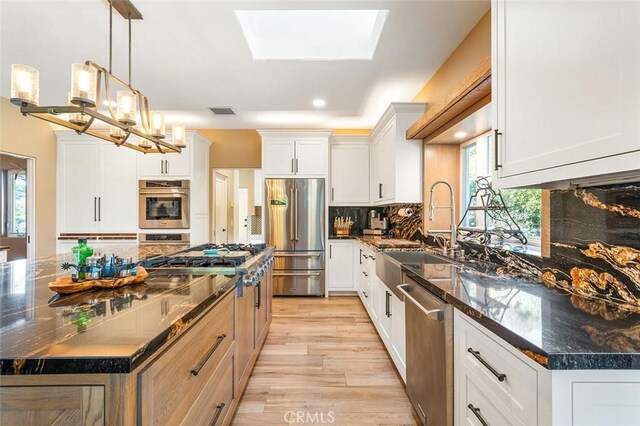 kitchen featuring a skylight, a kitchen island, appliances with stainless steel finishes, light hardwood / wood-style floors, and white cabinetry