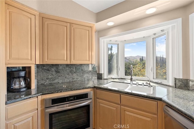 kitchen featuring sink, dark stone countertops, stainless steel appliances, tasteful backsplash, and light brown cabinetry