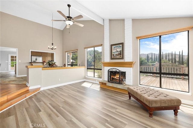 unfurnished living room featuring ceiling fan with notable chandelier, high vaulted ceiling, beamed ceiling, a brick fireplace, and light hardwood / wood-style flooring