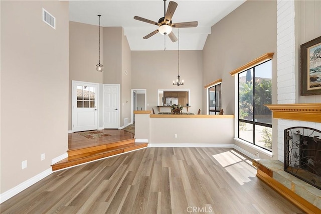 unfurnished living room with hardwood / wood-style flooring, a large fireplace, ceiling fan with notable chandelier, and high vaulted ceiling