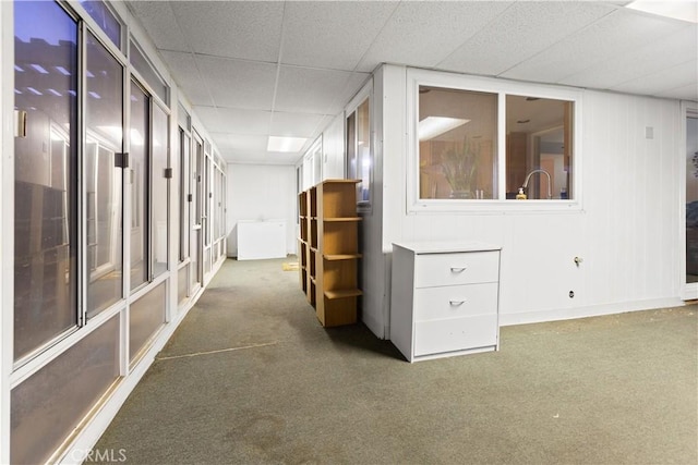 hall with dark colored carpet and a drop ceiling