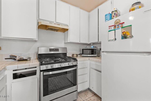 1431 Casa San Carlos Ln Unit A, Oxnard, CA 93033 - kitchen featuring stainless steel appliances, under cabinet range hood, tile countertops, white cabinets, and light tile patterned floors