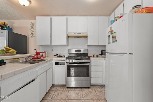 kitchen with sink, appliances with stainless steel finishes, tile counters, light tile patterned flooring, and white cabinetry