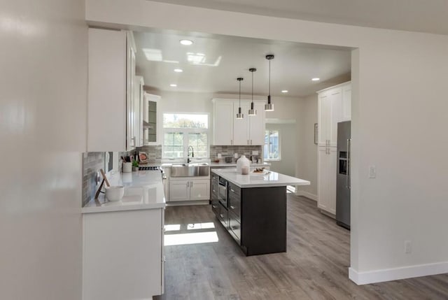 kitchen with hanging light fixtures, a center island, stainless steel fridge, decorative backsplash, and white cabinetry