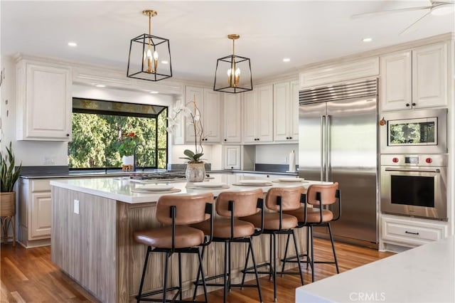 kitchen featuring white cabinetry, a center island, hanging light fixtures, built in appliances, and light wood-type flooring