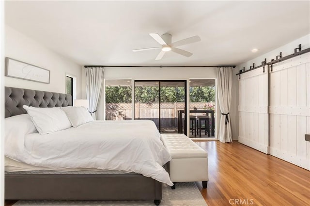 bedroom featuring ceiling fan, a barn door, wood-type flooring, and access to outside