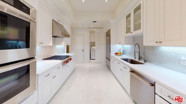 kitchen featuring sink, appliances with stainless steel finishes, tasteful backsplash, washer / dryer, and white cabinetry