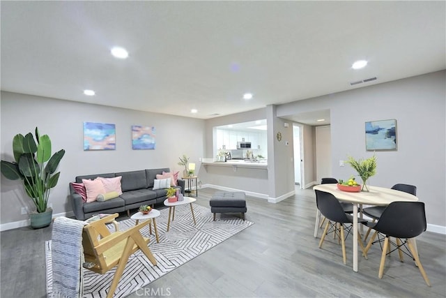 living room featuring baseboards, visible vents, wood finished floors, and recessed lighting