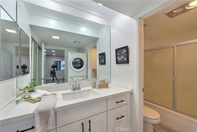 bathroom with stacked washer / drying machine, combined bath / shower with glass door, vanity, and toilet