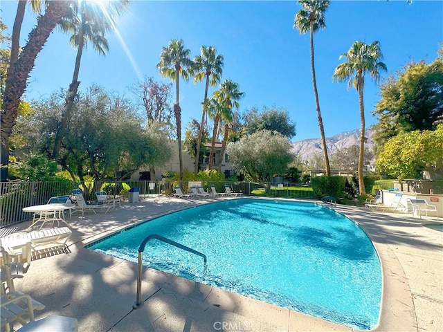 community pool with a patio area, fence, and a mountain view