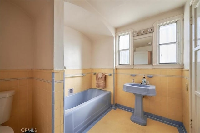 bathroom featuring a washtub, tile patterned floors, toilet, and tile walls