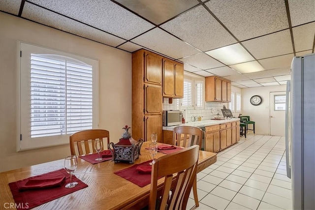 kitchen featuring decorative backsplash, white fridge, a drop ceiling, and light tile patterned flooring