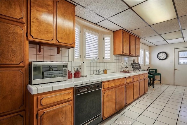 kitchen with sink, decorative backsplash, black dishwasher, tile counters, and light tile patterned flooring