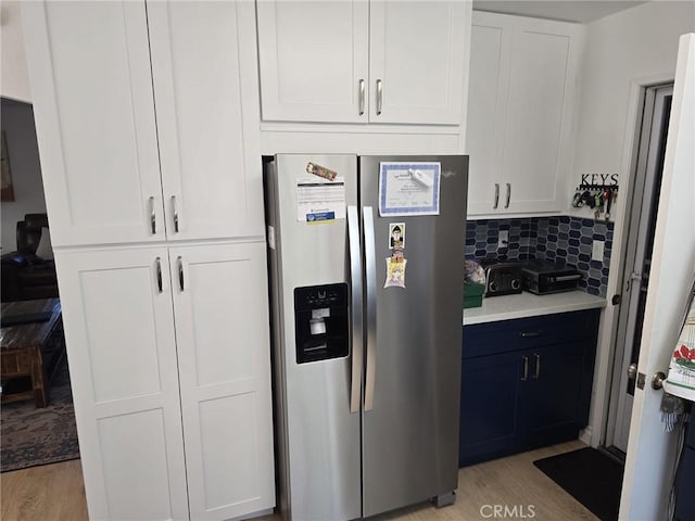 kitchen featuring decorative backsplash, stainless steel fridge, white cabinets, and light wood-type flooring