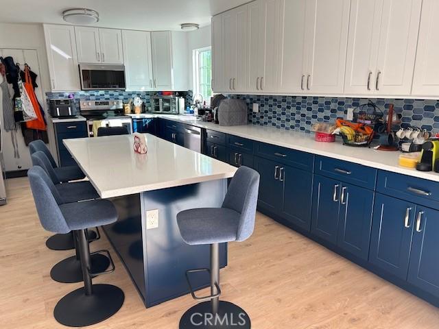 kitchen featuring blue cabinetry, a center island, a breakfast bar area, white cabinets, and appliances with stainless steel finishes