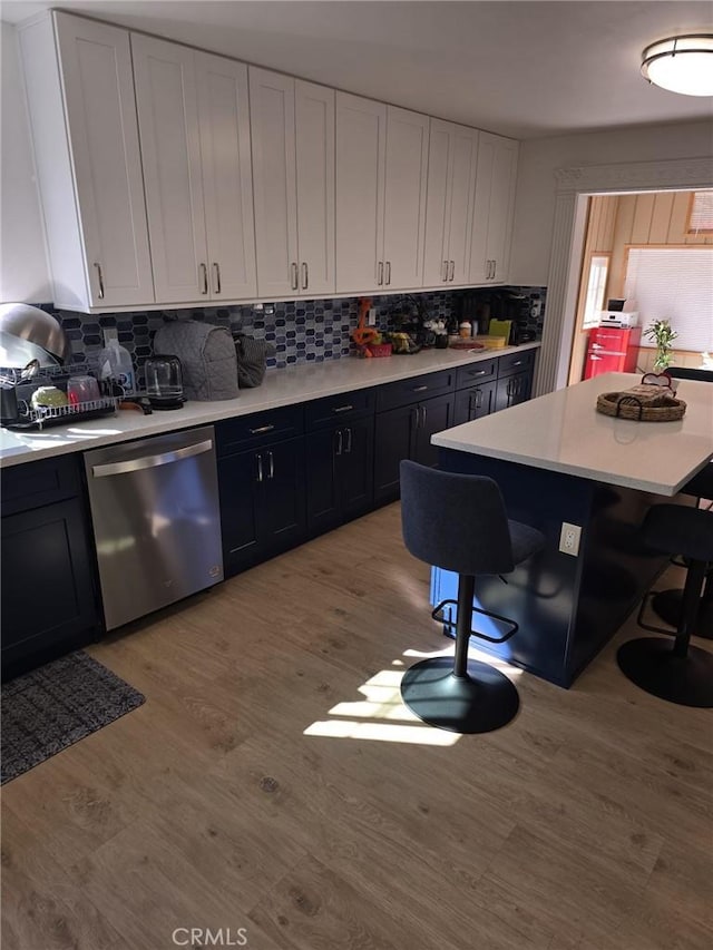 kitchen featuring dishwasher, backsplash, a kitchen breakfast bar, light wood-type flooring, and white cabinetry