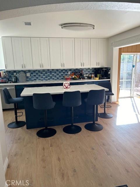 kitchen featuring decorative backsplash, stainless steel dishwasher, a breakfast bar, light hardwood / wood-style flooring, and white cabinets