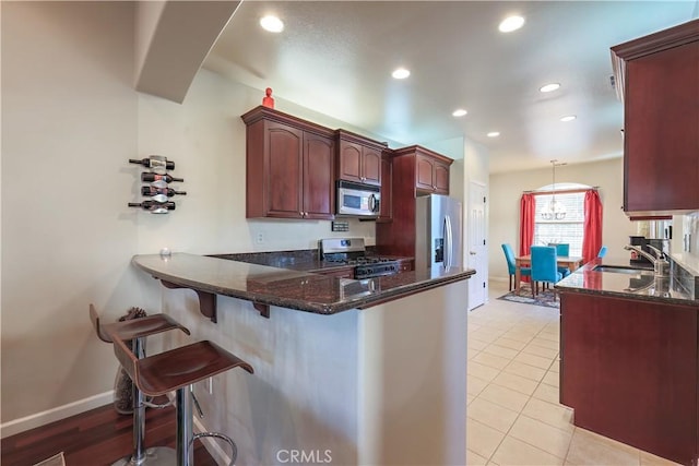 kitchen featuring sink, stainless steel appliances, kitchen peninsula, dark stone counters, and light tile patterned flooring