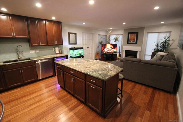 kitchen with dishwasher, sink, light hardwood / wood-style flooring, a breakfast bar area, and a kitchen island