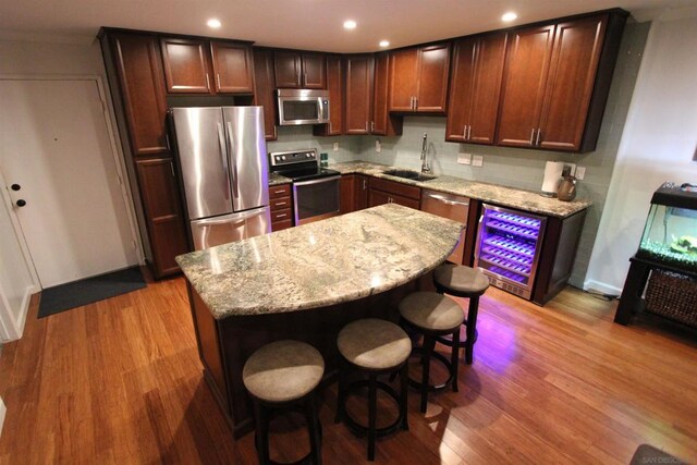 kitchen with sink, a kitchen island, light hardwood / wood-style floors, light stone counters, and stainless steel appliances