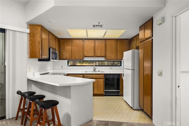 kitchen with sink, dishwasher, a kitchen breakfast bar, white refrigerator, and kitchen peninsula