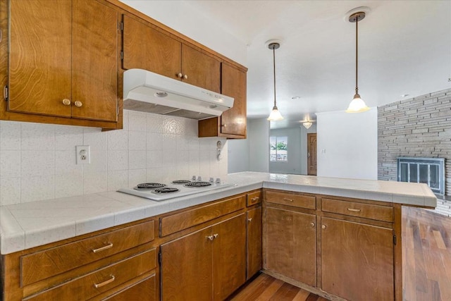 kitchen with pendant lighting, kitchen peninsula, decorative backsplash, white stovetop, and light wood-type flooring