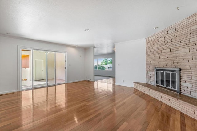 unfurnished living room featuring crown molding, wood-type flooring, and a stone fireplace