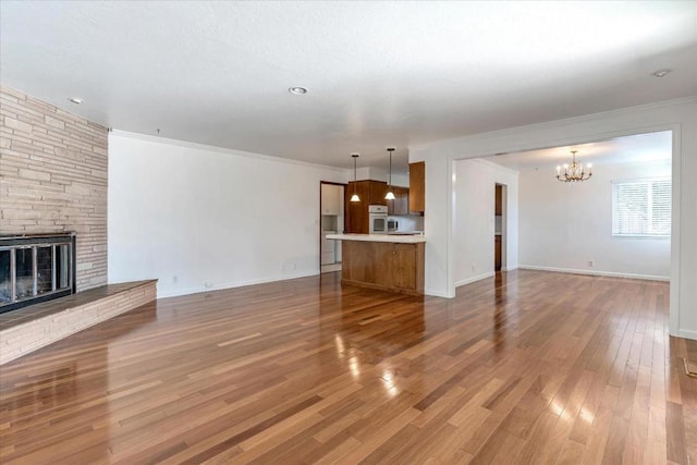 unfurnished living room with an inviting chandelier, ornamental molding, hardwood / wood-style flooring, and a stone fireplace