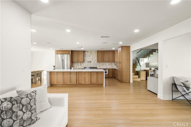 kitchen featuring a kitchen island with sink, light hardwood / wood-style flooring, tasteful backsplash, and stainless steel refrigerator