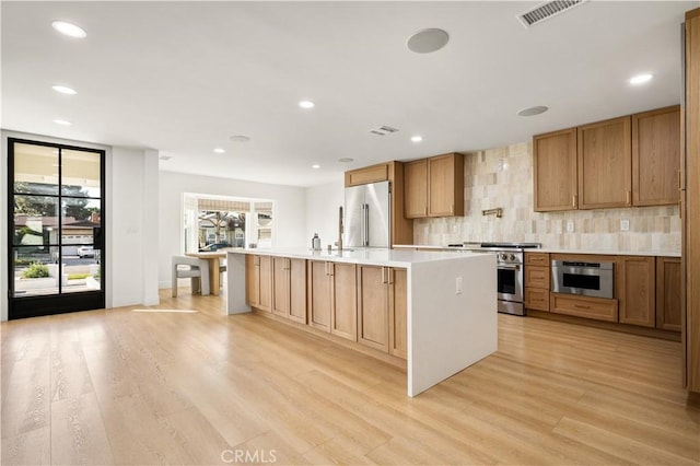 kitchen featuring light hardwood / wood-style floors, premium appliances, backsplash, and an island with sink