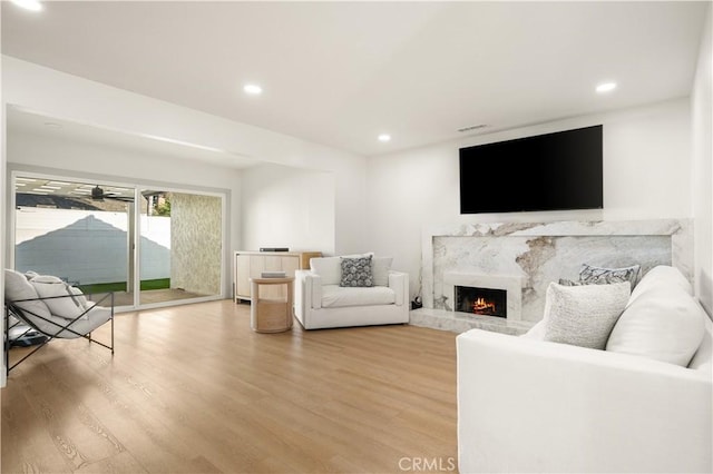 living room with ceiling fan, wood-type flooring, and a premium fireplace