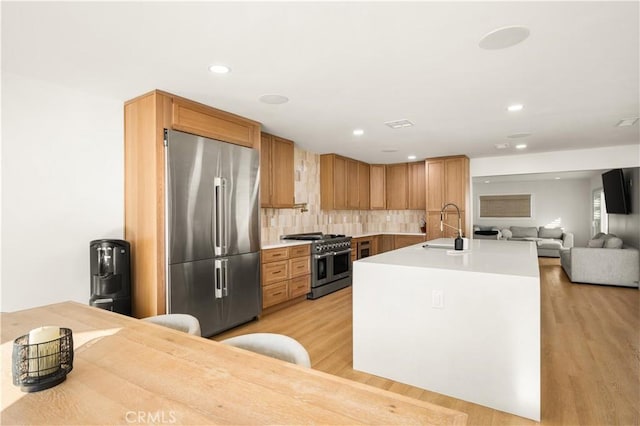 kitchen featuring high end appliances, decorative backsplash, light wood-type flooring, and sink