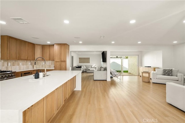 kitchen featuring a spacious island, high end stainless steel range, sink, backsplash, and light hardwood / wood-style flooring