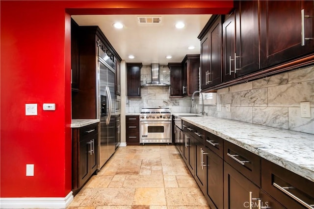 kitchen with stainless steel stove, sink, decorative backsplash, light stone counters, and wall chimney exhaust hood