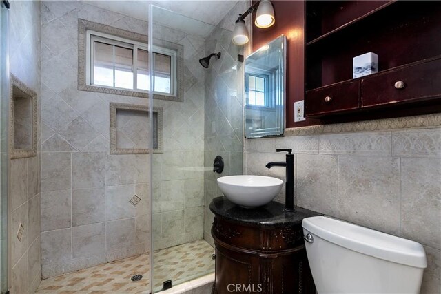 bathroom with toilet, vanity, tile walls, backsplash, and a shower with shower door