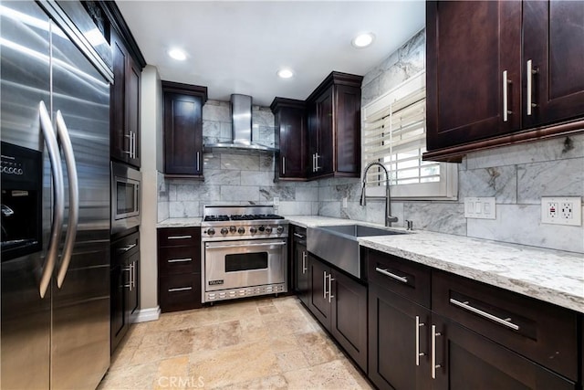 kitchen featuring decorative backsplash, wall chimney range hood, light stone counters, built in appliances, and sink