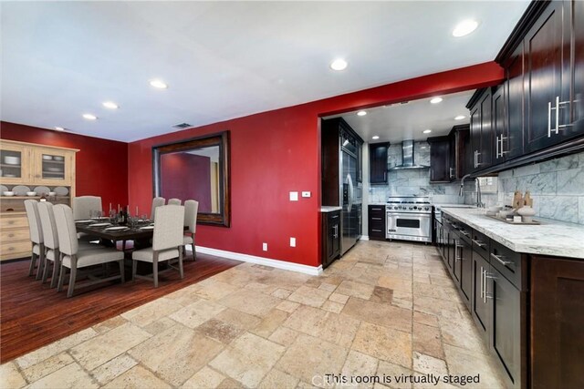 kitchen with premium appliances, wall chimney exhaust hood, decorative backsplash, sink, and light stone counters