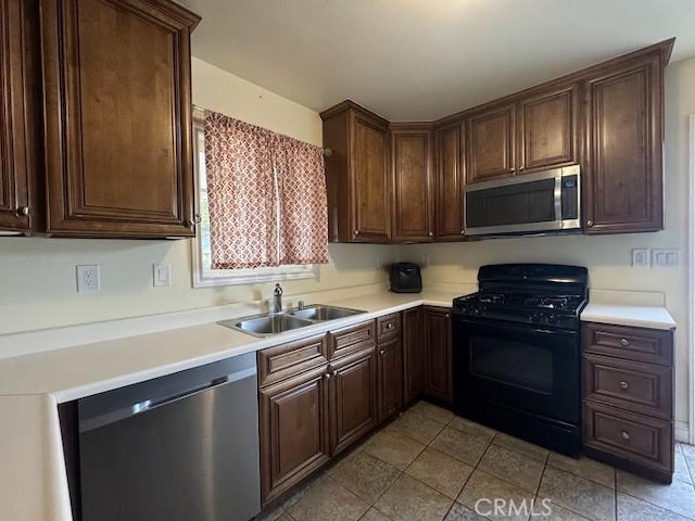 kitchen with appliances with stainless steel finishes, light tile patterned floors, dark brown cabinets, and sink