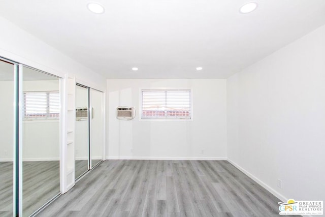 spare room with a wall mounted AC, light wood-type flooring, and a wealth of natural light