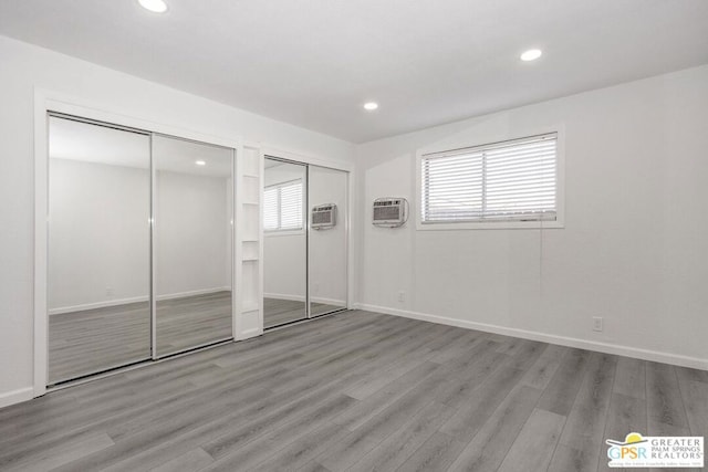 unfurnished bedroom with light wood-type flooring, multiple closets, and a wall mounted AC