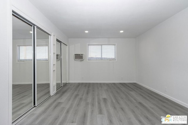 unfurnished bedroom featuring light wood-type flooring, multiple closets, and a wall mounted air conditioner