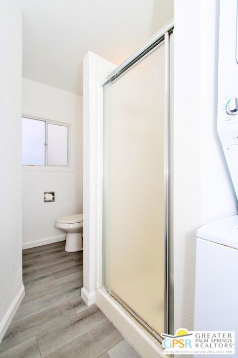 bathroom featuring toilet, a shower with shower door, and hardwood / wood-style flooring