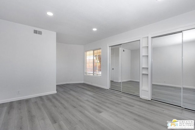 unfurnished bedroom featuring multiple closets and light hardwood / wood-style floors