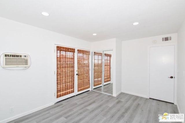 unfurnished bedroom featuring an AC wall unit, light hardwood / wood-style floors, and access to exterior