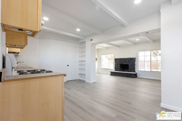 kitchen featuring beam ceiling, light brown cabinets, a stone fireplace, and light hardwood / wood-style floors