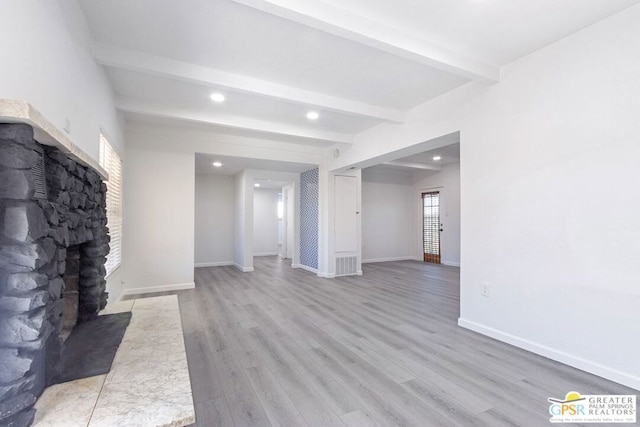 unfurnished living room with beam ceiling, light hardwood / wood-style flooring, and a stone fireplace