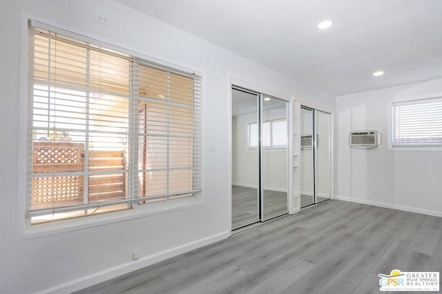 unfurnished bedroom featuring an AC wall unit, two closets, and light wood-type flooring